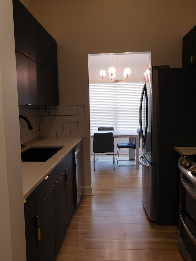 kitchen with appliances with stainless steel finishes, tasteful backsplash, sink, hanging light fixtures, and light hardwood / wood-style flooring