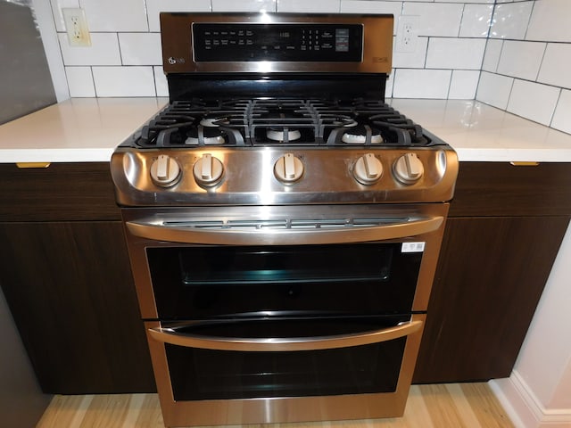 interior details featuring dark brown cabinets, light wood-type flooring, range with two ovens, and backsplash