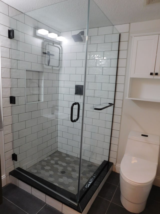 bathroom featuring a shower with shower door, tile patterned floors, toilet, and a textured ceiling