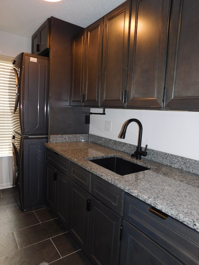 kitchen featuring plenty of natural light, stacked washing maching and dryer, light stone countertops, and sink