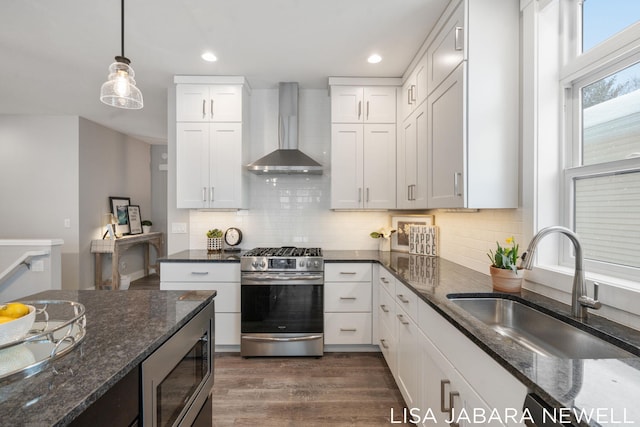 kitchen featuring dark stone countertops, wall chimney exhaust hood, stainless steel appliances, and white cabinets