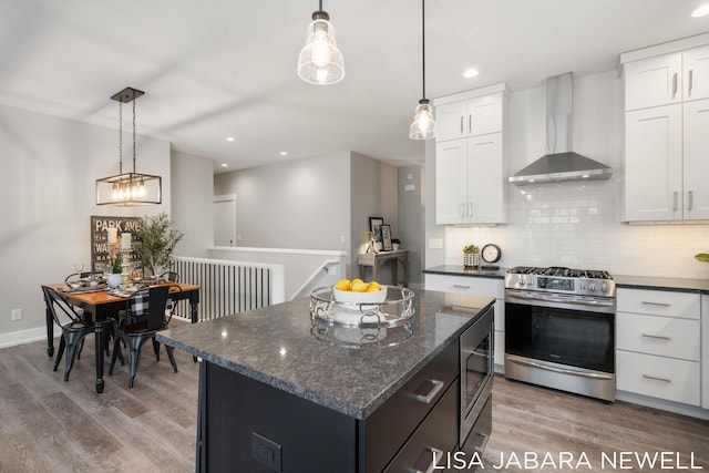 kitchen with appliances with stainless steel finishes, white cabinetry, a kitchen island, decorative light fixtures, and wall chimney exhaust hood