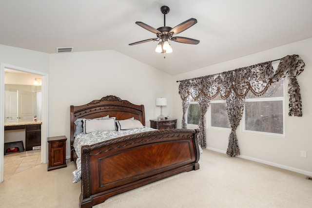 bedroom with vaulted ceiling, light colored carpet, ceiling fan, and ensuite bath