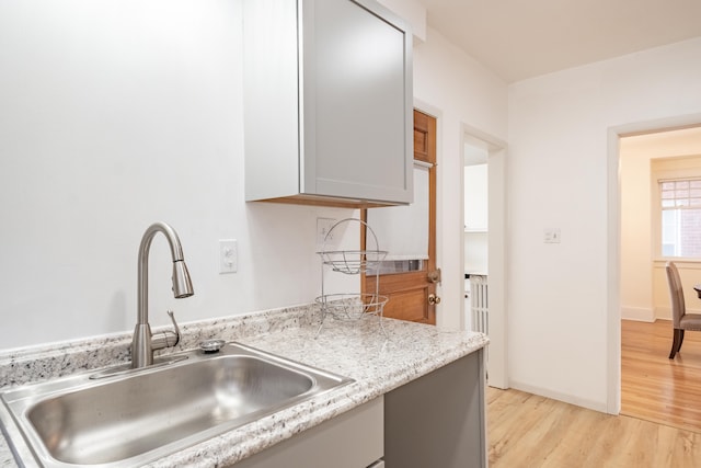 kitchen with light stone counters, sink, light hardwood / wood-style floors, and gray cabinetry