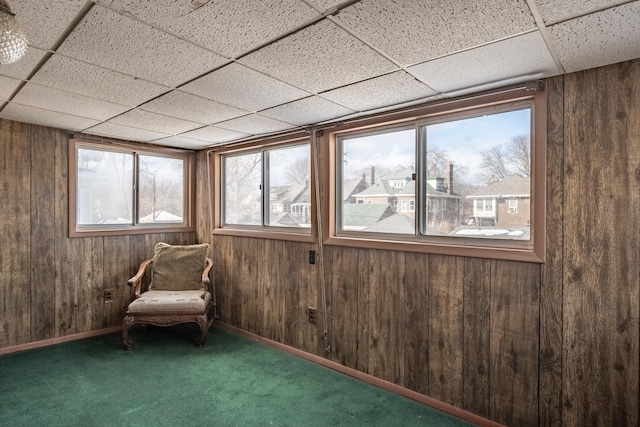 unfurnished room featuring a drop ceiling, dark carpet, and wood walls