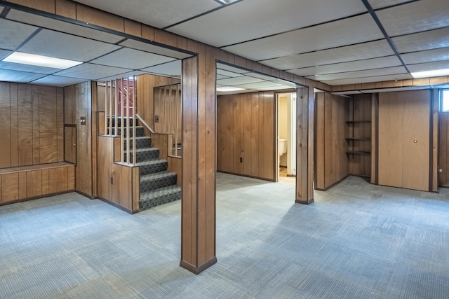 basement featuring a drop ceiling and wooden walls