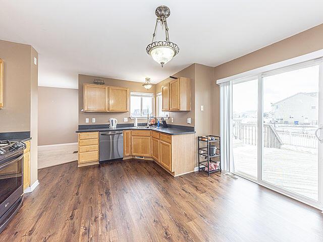 kitchen featuring stainless steel appliances, dark hardwood / wood-style floors, light brown cabinetry, and hanging light fixtures