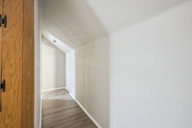 corridor with hardwood / wood-style flooring and vaulted ceiling