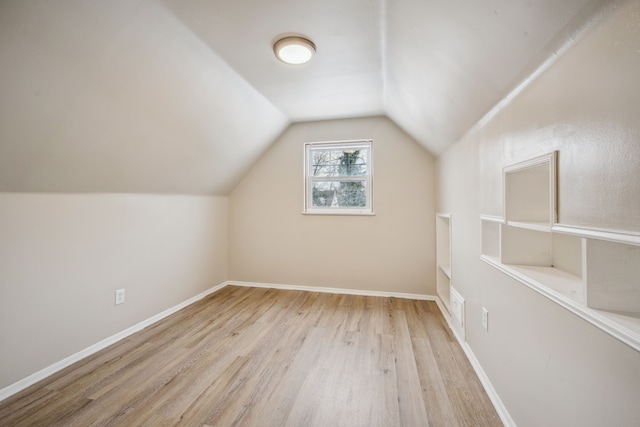 additional living space with vaulted ceiling, light hardwood / wood-style floors, and built in shelves