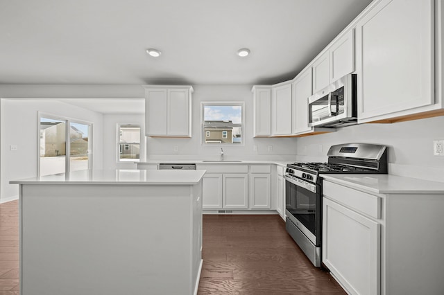 kitchen with a kitchen island, light countertops, stainless steel appliances, white cabinetry, and dark wood-style flooring