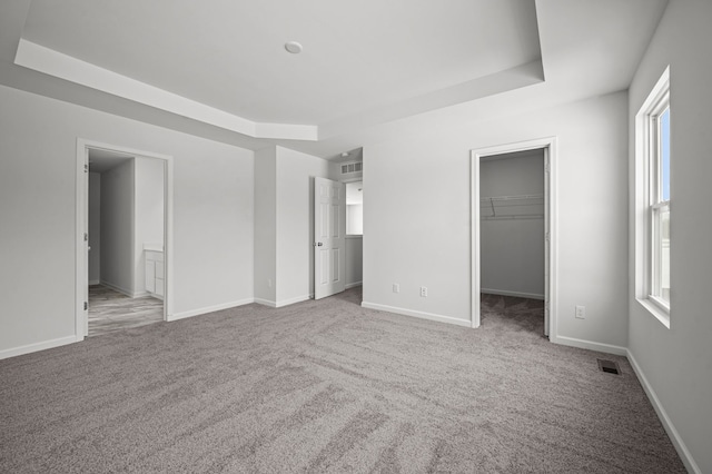 unfurnished bedroom with a tray ceiling, carpet, and visible vents