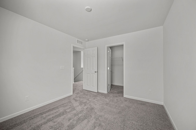 unfurnished bedroom featuring visible vents, a walk in closet, baseboards, carpet floors, and a closet