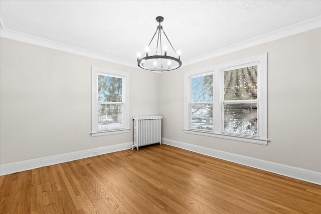 spare room featuring ornamental molding, wood-type flooring, radiator, and a notable chandelier