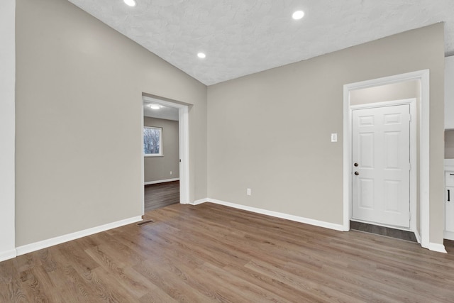 empty room with light hardwood / wood-style flooring, a textured ceiling, and vaulted ceiling