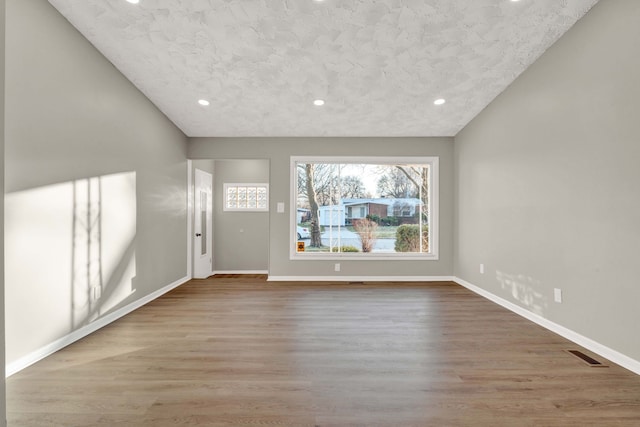 unfurnished living room with hardwood / wood-style flooring, lofted ceiling, and a textured ceiling