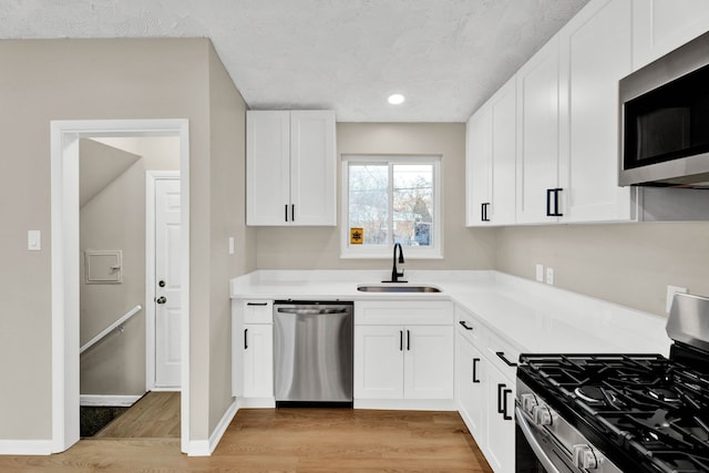 kitchen featuring sink, stainless steel appliances, light hardwood / wood-style floors, a textured ceiling, and white cabinets