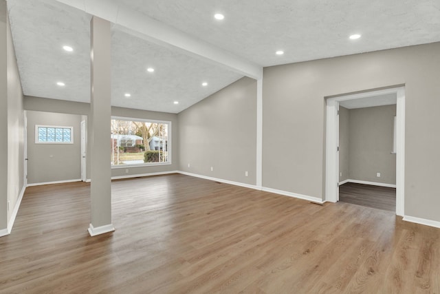 unfurnished living room with light hardwood / wood-style floors, lofted ceiling with beams, and a textured ceiling