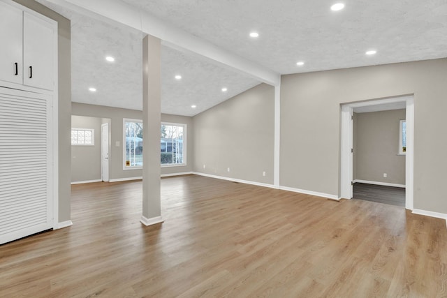 unfurnished living room with vaulted ceiling with beams, a textured ceiling, and light hardwood / wood-style flooring