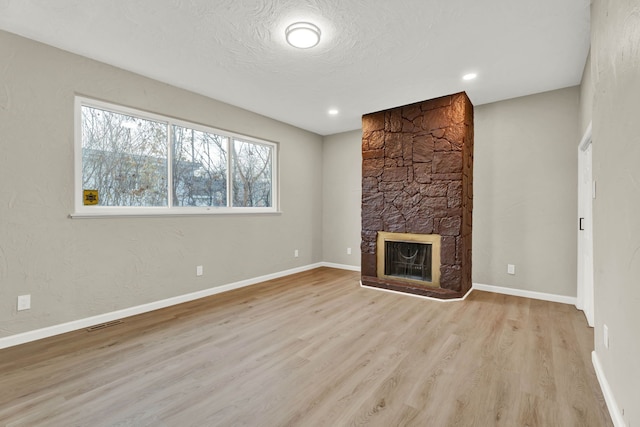 unfurnished living room featuring a stone fireplace, light hardwood / wood-style floors, and a textured ceiling