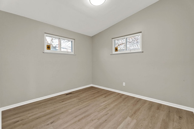 spare room featuring vaulted ceiling, light hardwood / wood-style floors, and a healthy amount of sunlight