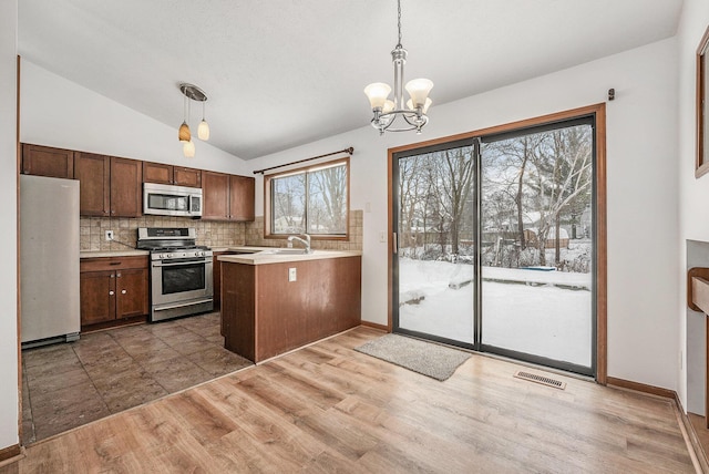 kitchen with pendant lighting, vaulted ceiling, kitchen peninsula, and appliances with stainless steel finishes