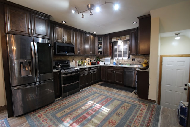 kitchen featuring sink, wood-type flooring, dark brown cabinets, appliances with stainless steel finishes, and decorative backsplash