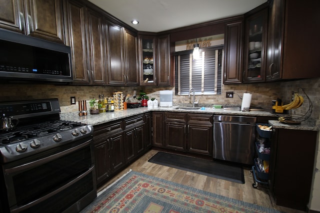 kitchen with light stone counters, dark brown cabinetry, appliances with stainless steel finishes, and sink