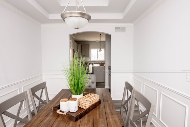 dining space with arched walkways, wood finished floors, a raised ceiling, and visible vents