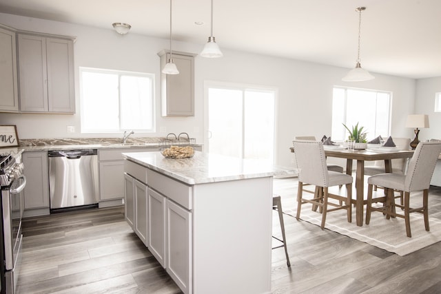 kitchen with gray cabinetry, appliances with stainless steel finishes, a kitchen island, light stone countertops, and light wood-type flooring