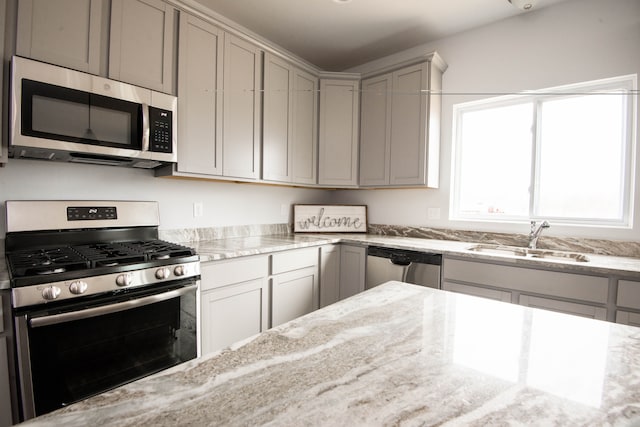 kitchen featuring appliances with stainless steel finishes, a sink, light stone counters, and gray cabinetry