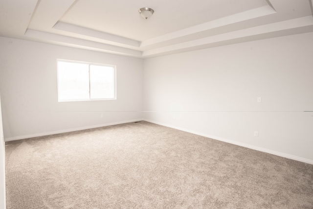 carpeted empty room featuring a tray ceiling and baseboards