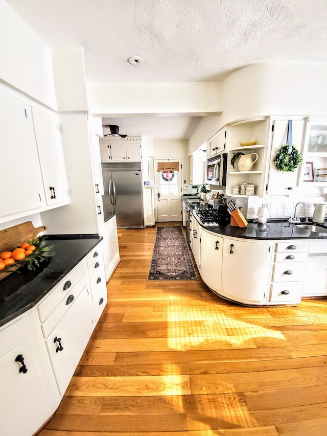 kitchen with sink, white cabinetry, stainless steel appliances, light hardwood / wood-style floors, and a textured ceiling