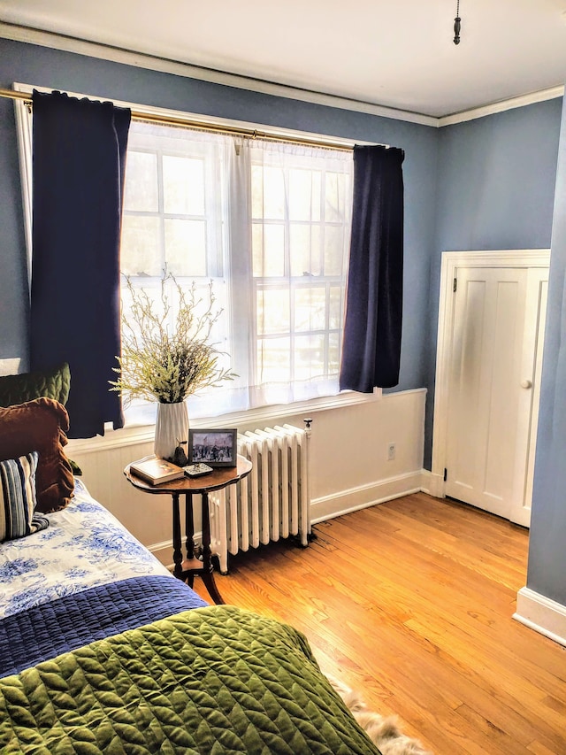 bedroom featuring crown molding, radiator heating unit, and light hardwood / wood-style flooring