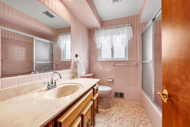 full bathroom featuring toilet, combined bath / shower with glass door, tile walls, vanity, and tile patterned flooring