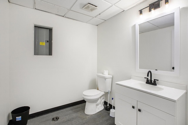 bathroom with hardwood / wood-style floors, a paneled ceiling, vanity, electric panel, and toilet