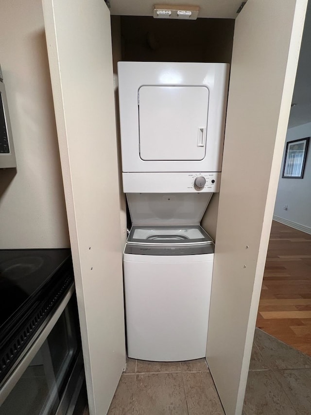 laundry area with stacked washer / drying machine, laundry area, baseboards, and wood finished floors