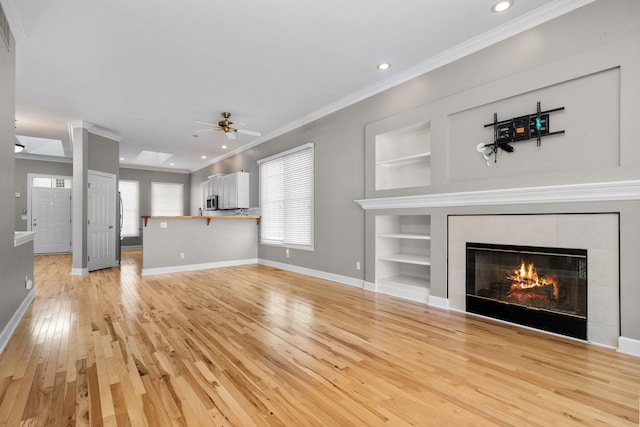 unfurnished living room with built in features, a fireplace, ceiling fan, light hardwood / wood-style floors, and crown molding