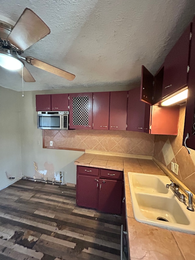 kitchen featuring tile countertops, sink, decorative backsplash, ceiling fan, and a textured ceiling