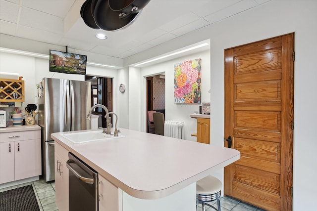 kitchen featuring sink, radiator heating unit, an island with sink, white cabinets, and a kitchen bar