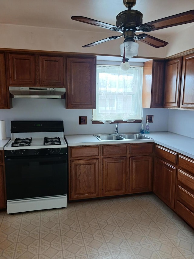 kitchen featuring light countertops, ceiling fan, a sink, gas range, and under cabinet range hood