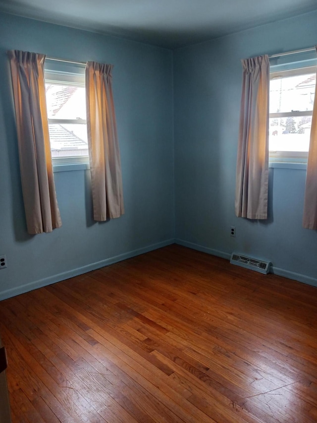 unfurnished room with hardwood / wood-style floors, baseboards, visible vents, and a wealth of natural light