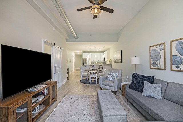 living room with light hardwood / wood-style floors, a barn door, and ceiling fan