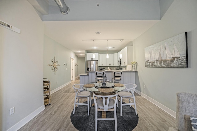 dining space with rail lighting and light wood-type flooring