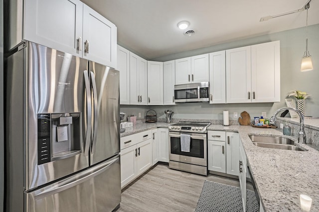 kitchen featuring decorative light fixtures, white cabinetry, sink, stainless steel appliances, and light stone countertops