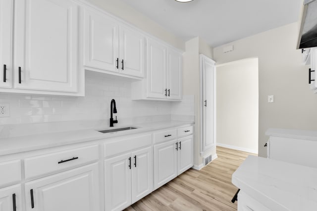 kitchen featuring light stone counters, sink, light hardwood / wood-style floors, and white cabinets