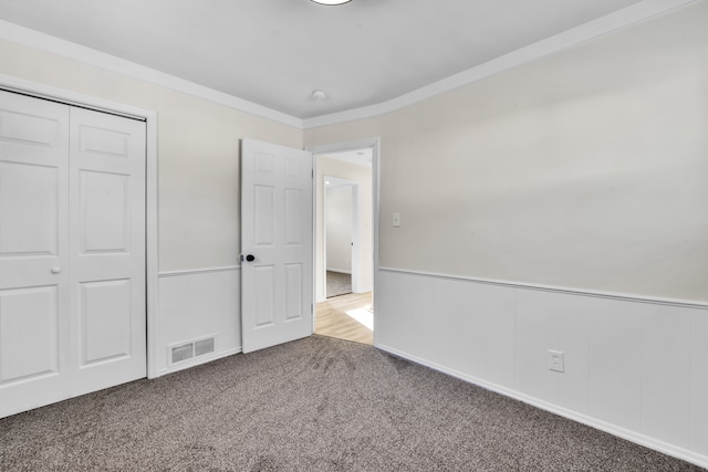 unfurnished bedroom with ornamental molding, a closet, and carpet flooring