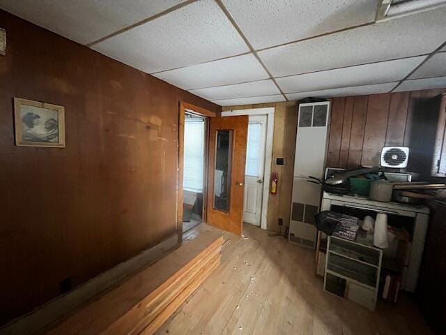 interior space with a drop ceiling, light wood-type flooring, and wood walls