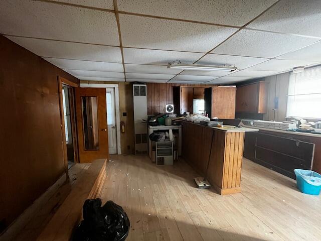 kitchen with a paneled ceiling, wooden walls, and light hardwood / wood-style flooring