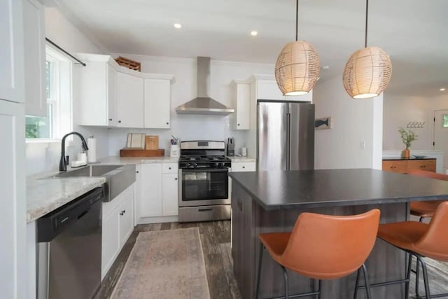 kitchen featuring wall chimney range hood, sink, white cabinetry, stainless steel appliances, and decorative light fixtures