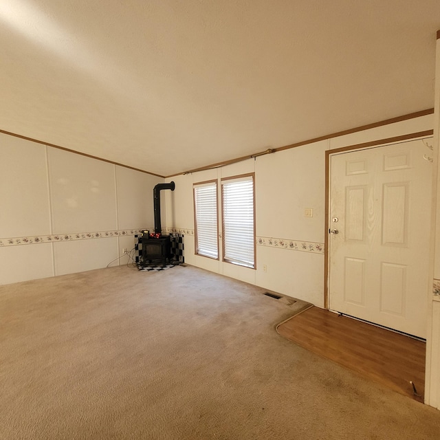 unfurnished living room featuring crown molding, carpet floors, and a wood stove